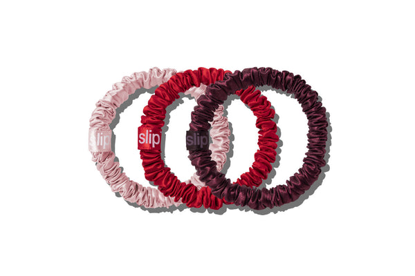 Three pure silk scrunchies in light pink, deep red, and dark burgundy, arranged in an overlapping circle on a white background.