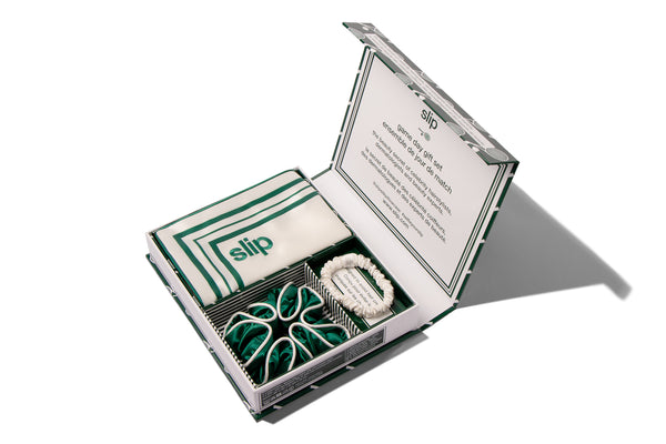 Open box containing a silk pillowcase, a green silk scrunchie and a white silk scrunchie with slip branding on a white background
