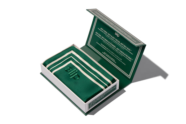 Open box containing green silk pillowcase with white piping, on a white background