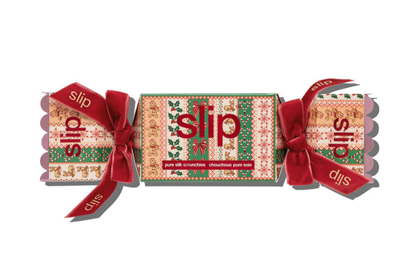 A Christmas-themed scrunchie cracker in festive patterned packaging with red ribbon bows and the brand name 'slip' printed on the sides, isolated on a white background.
