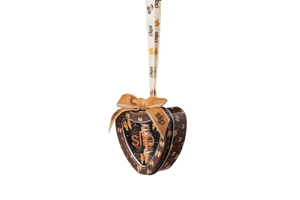 A heart-shaped metal gift tin with a hanging ribbon, featuring a bow design and the brand name 'slip' printed on the lid and ribbon, set against a plain white background.