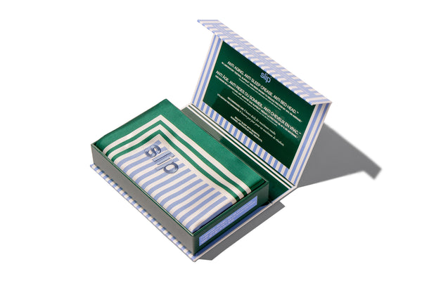 Opened box containing a blue, white and green striped silk pillowcase with slip logo embroidered, on a white background