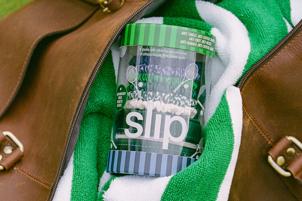 Clear slip packaging containing slip scrunchies with green lid inside a brown leather bag with a green towel.